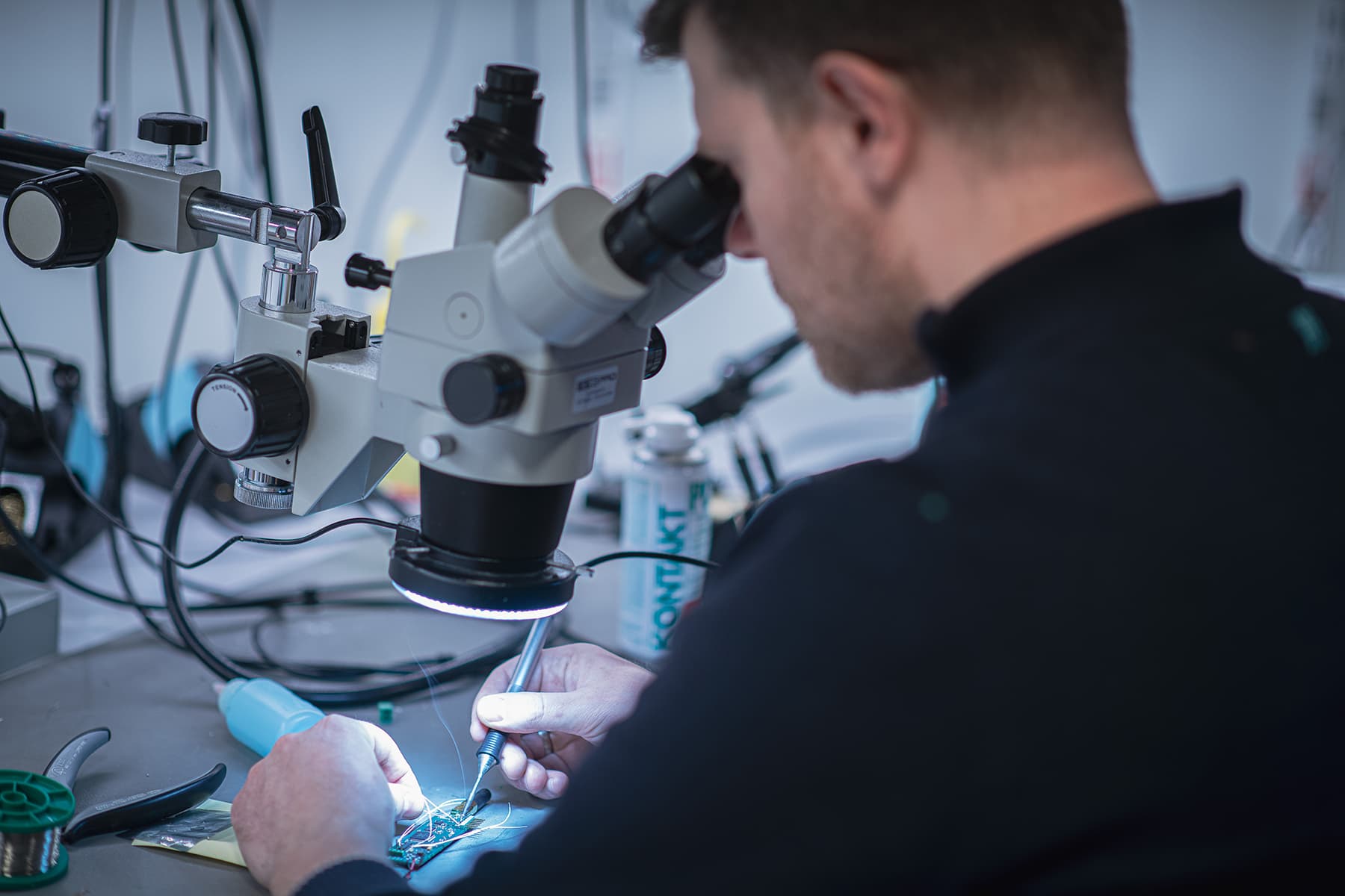 An engineer soldering a small circuit board under a microscope.