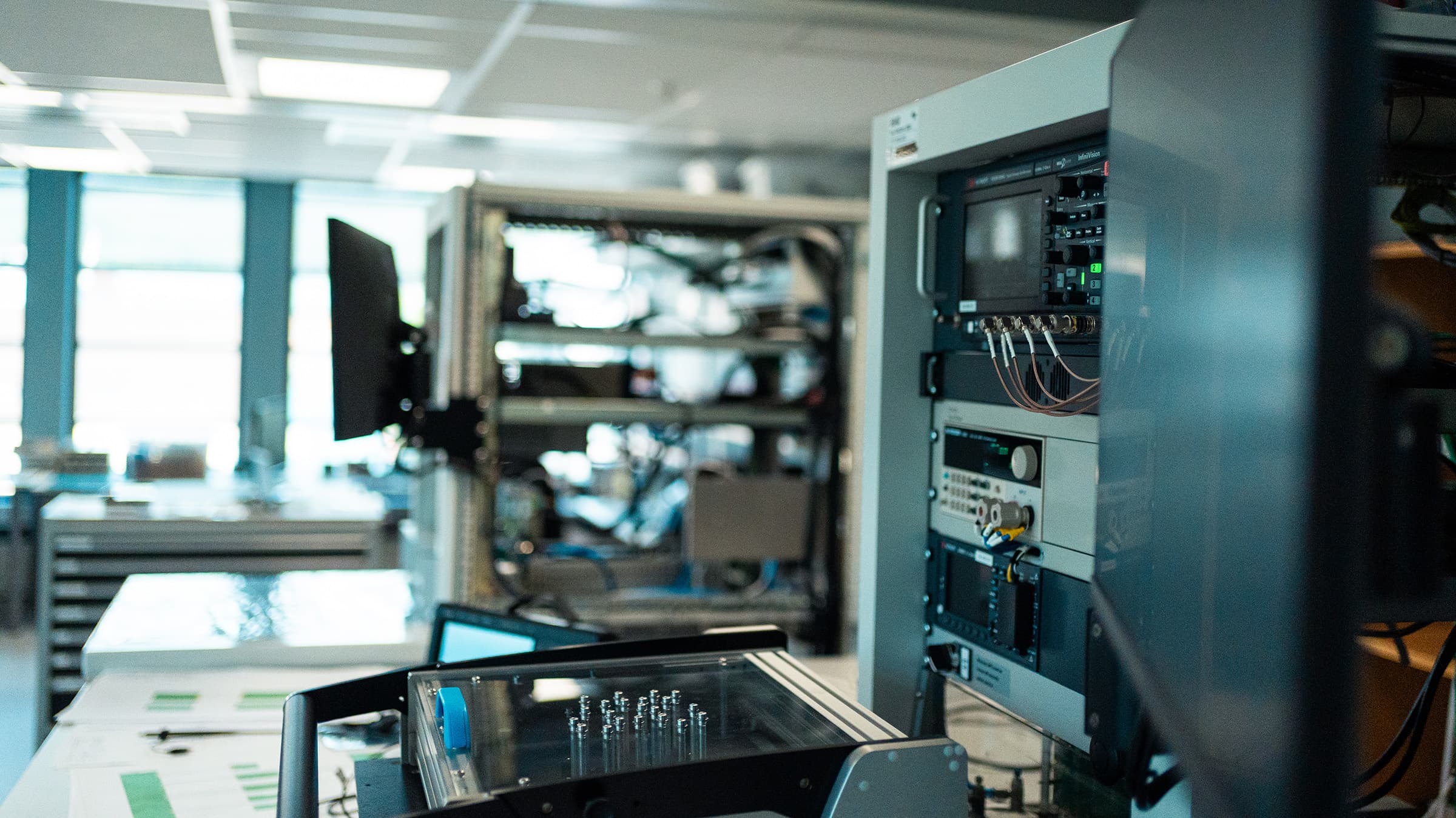 A test rack with oscilloscope and power supply, a test fixture in the foreground.